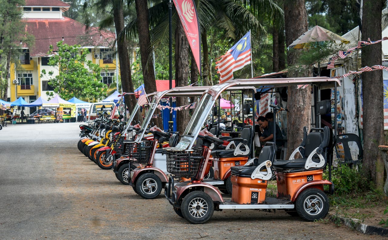 Electric scooters and motorcycles are parked along a market street in Malaysia.
